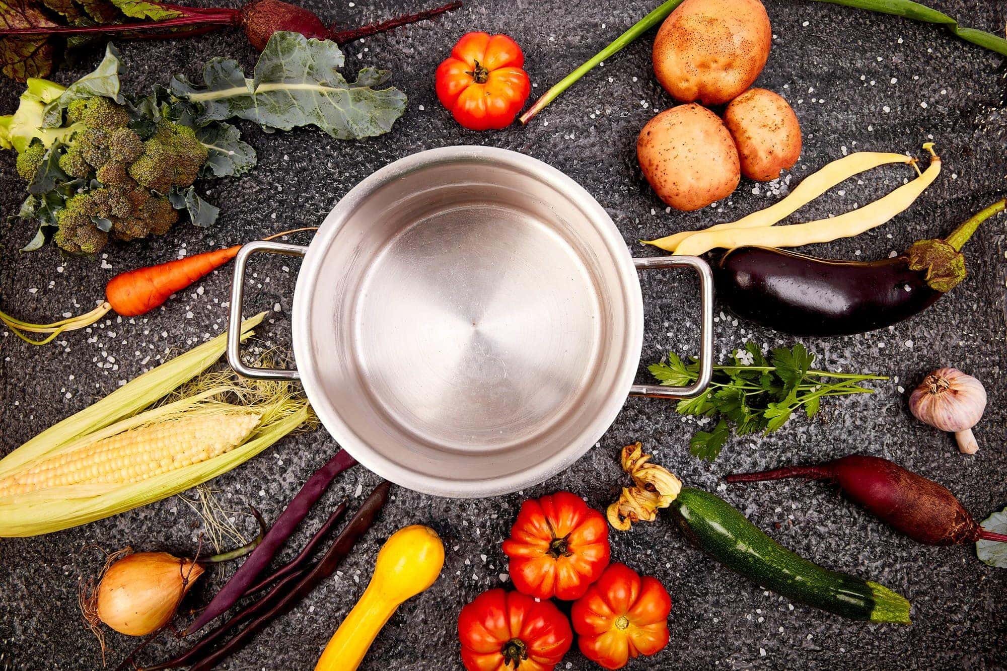 Various organic vegetables ingredients around empty cooking pot